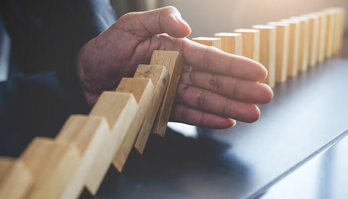 Strategies for effective risk mitigation - tycoonstory | tycoonstory media Hand stopping falling dominoes in a line, representing risk mitigation and prevention of cascading problems.