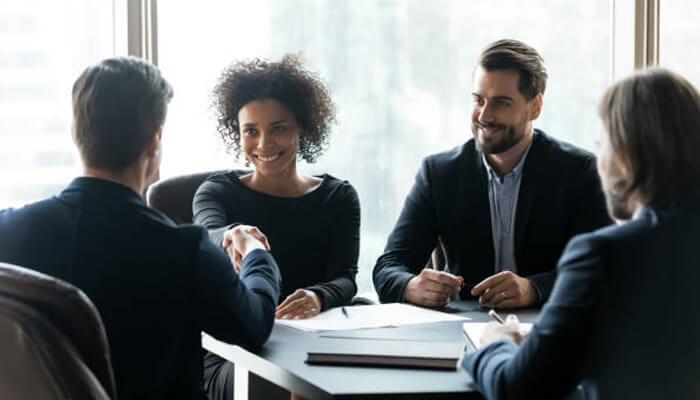 10 ways gratitude can help create better business owner Business professionals shaking hands, smiling, and exchanging gratitude during a meeting, highlighting appreciation in professional relationships.