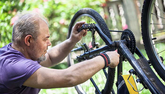Check the gears and shifters A close-up of a man performing maintenance on a mountain bicycle, specifically working on the pedal and drivetrain area while the bike is positioned upside down for easier repair.