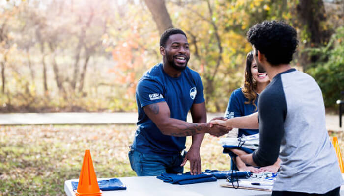Community involvement Community involvement in action as a volunteer greets a participant at an outdoor event booth, highlighting local outreach, support initiatives, and volunteer service.