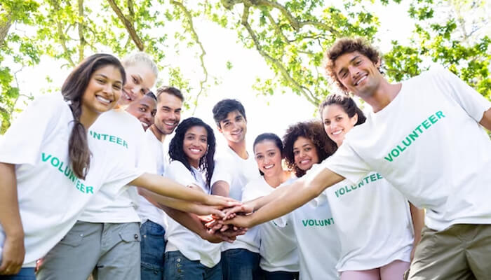 Community involvement Community involvement captured as smiling volunteers in matching shirts stacking hands together outdoors, representing collaboration, charity work, and civic engagement.