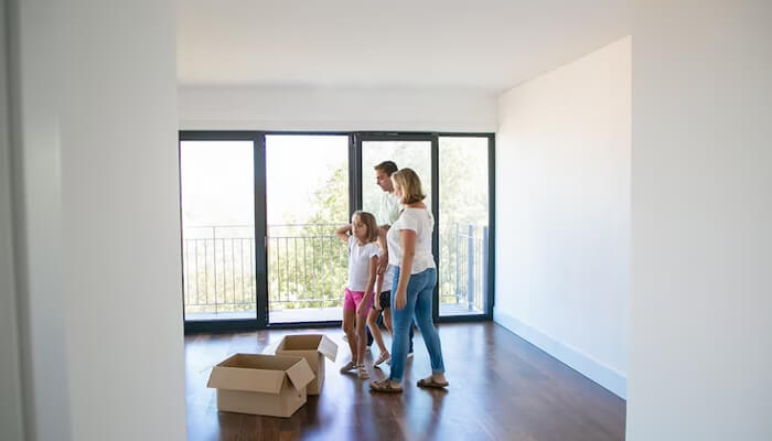 Popular areas for 1 bhk flat rentals in delhi Family walking through an empty room of a new home, preparing to move into their new space with cardboard boxes nearby.