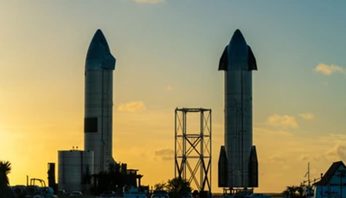 Spacecraft Two large spacecraft standing on a launchpad silhouetted against a golden sunset, representing the preparation and long-term goals set this monday.