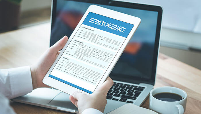 Insurance A person reviewing a business insurance form on a tablet while working on their laptop, representing the importance of insurance for an online business.