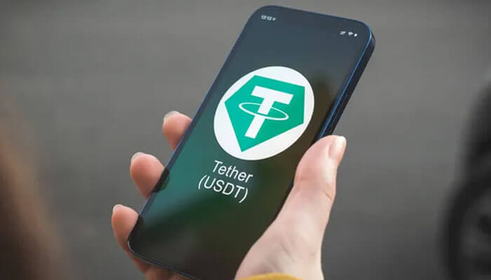 Tether-tycoonstory | tycoonstory media Hand holding a smartphone displaying the tether usdt logo, depicting stablecoin usage in the crypto casino market.