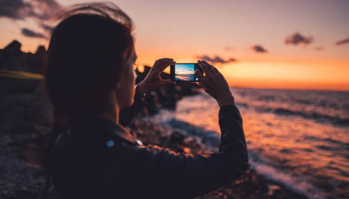 The ultimate guide to merging photos on your iphone A person capturing a scenic sunset with an iphone, showing how to combine photos on iphone in the editing section.