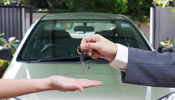 Advantages of buying used cars Seller handing car keys to a buyer in front of a vehicle, symbolizing ownership transfer and purchase of a used car.