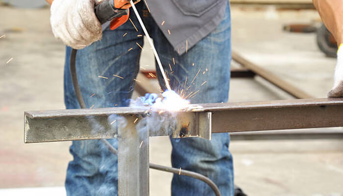 Good for thick metals Close up of a worker in jeans using an electrode to perform stick welding on a piece of metal, creating sparks.