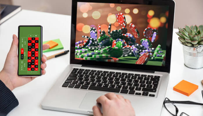 How to earn money by playing online cash games on getmega Person playing an online casino game on their laptop and mobile phone, with a background of casino chips and roulette.