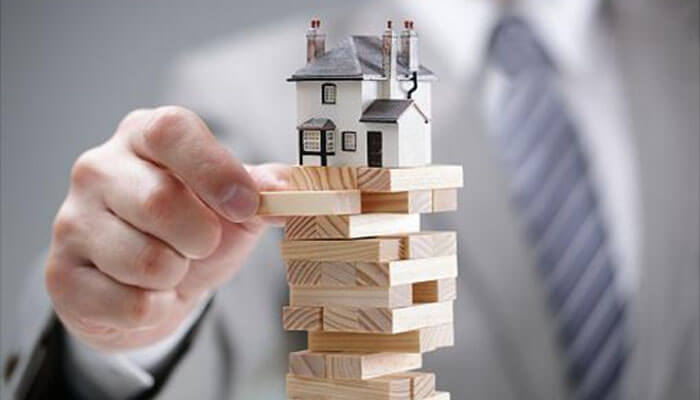How to start a rental property business during recession Person carefully balancing a miniature house on top of wooden blocks, representing the delicate balance required in managing a rental property business.