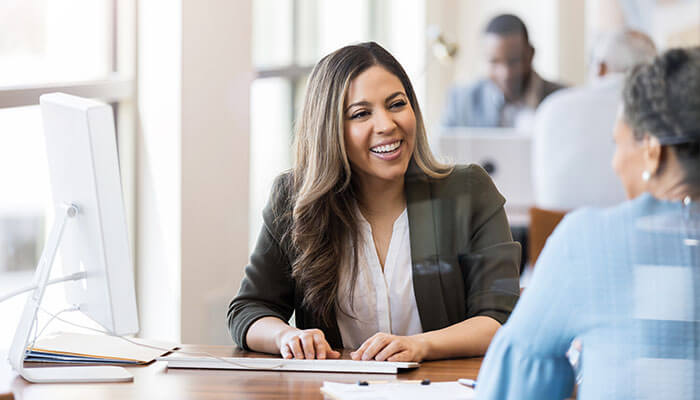 Open a demat account - tycoonstory | tycoonstory media A business professional smiling while discussing online trading options with a client in an office setting.