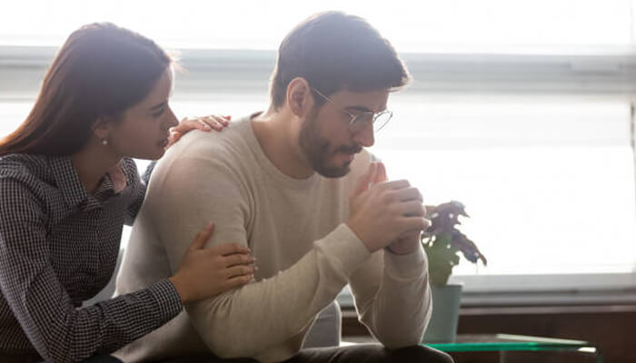 Seek support A concerned woman comforting a distressed man sitting with his hands clasped, symbolizing emotional support for someone struggling with alcoholism.
