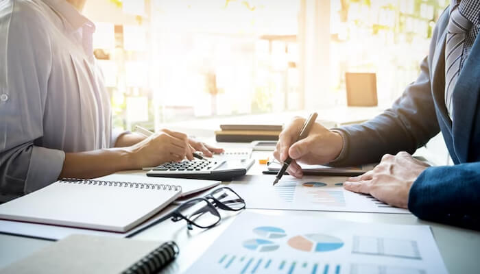 What is a financial controller Two financial controllers working together on a financial report, using a calculator and pen to analyze charts and data for strategic decisions.