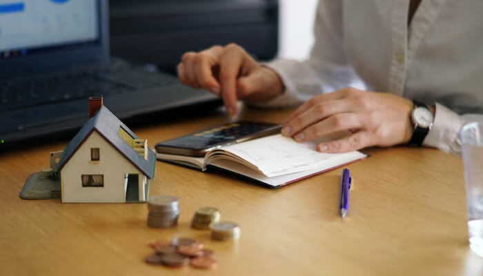 Pergola uses Pergola construction budgeting represented by a miniature house, coins, and a person calculating costs.