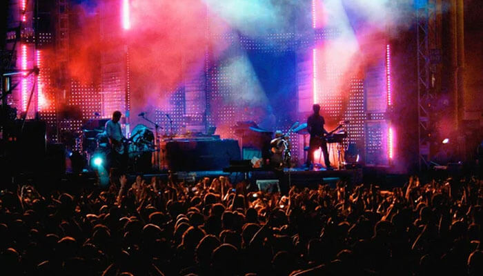 Beijing A vibrant live music concert in beijing, with colorful stage lights and smoke illuminating the band while a large crowd of fans raises their hands in front of the stage.