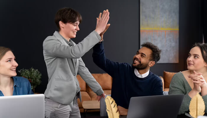Employee recognition | tycoonstory media Employees giving a high-five to celebrate teamwork and employee recognition in a modern office environment.