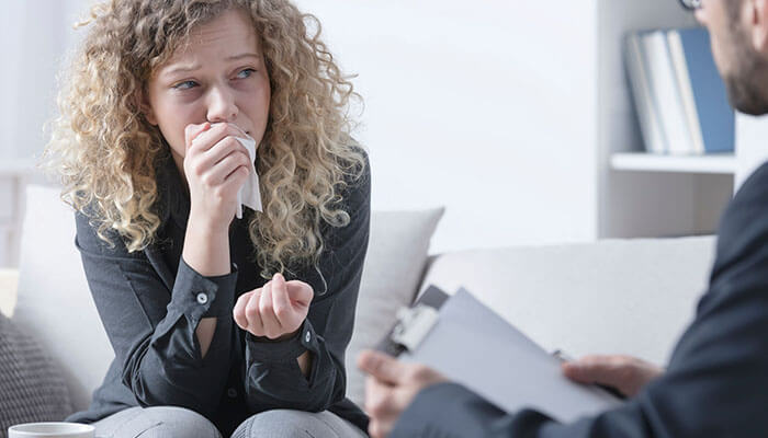 Create a bereavement leave policy - tycoonstory | tycoonstory media A concerned woman speaking with a professional counselor while holding a tissue, representing supporting employees through mental health support and compassionate workplace care.