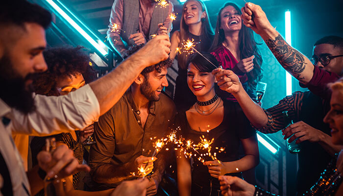 Losing interest A group of people celebrating at a party, with some individuals holding sparklers, where a few appear distracted or disengaged, reflecting signs of losing interest in the social gathering.