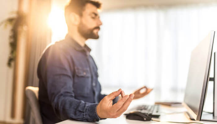 Meditation - tycoonstory | tycoonstory media A stressed entrepreneur meditating at his desk to manage entrepreneurial burnout while working on a computer.