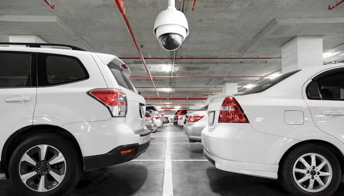 Park in secured locations The image shows a secured indoor parking lot with a ceiling-mounted security camera, highlighting car theft prevention and safe parking measures.