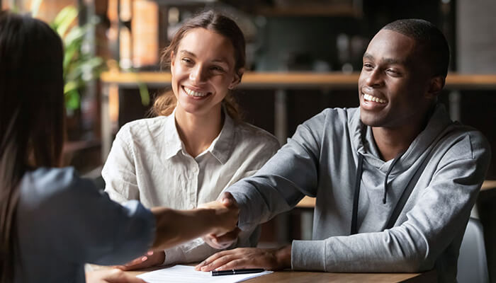 Unsecured business loans A smiling couple shaking hands with a loan officer while discussing unsecured business loans at a coffee shop or casual meeting place.