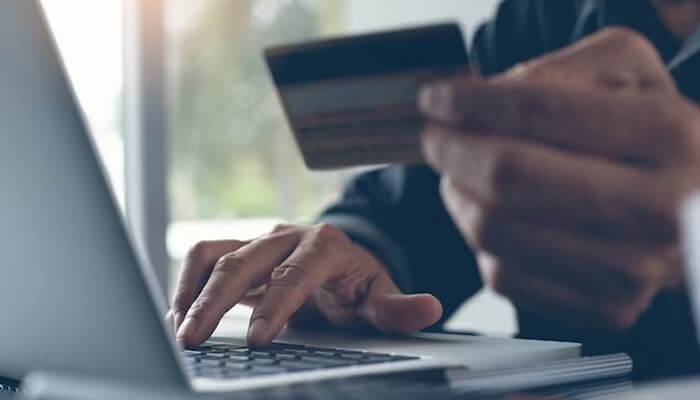 Ways to check transaction history through a pnb mini statement A person holding a bank card while typing on a laptop, symbolizing online banking activities such as viewing a pnb mini statement.