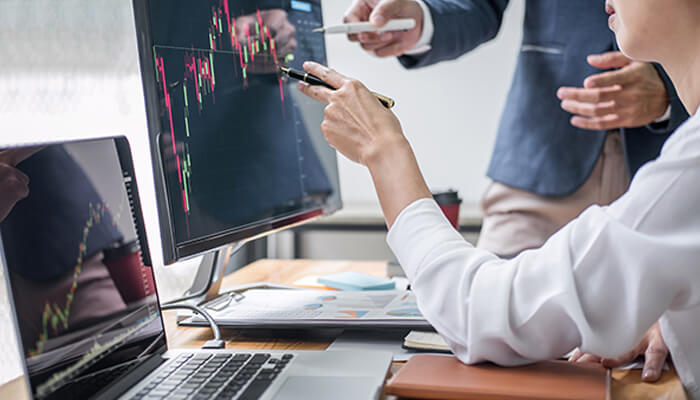 True forex funds Two professionals discussing forex market trends on a monitor, analyzing data and charts as part of their investment strategies with true forex funds.