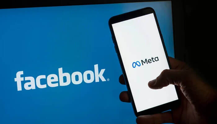 Facebook Hand holding a smartphone showing the meta logo in front of a screen displaying the facebook logo, highlighting facebook’s parent company.