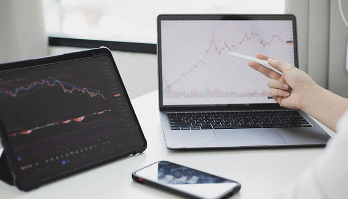 Trading A person analyzing trading charts on multiple screens, comparing data on a tablet and laptop to make informed trading decisions.