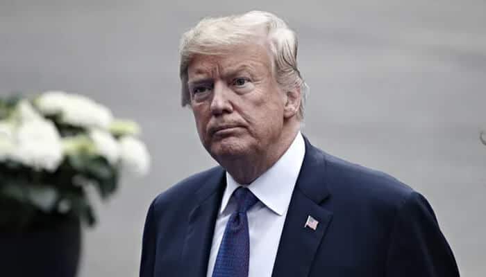 Trump Close-up portrait of a senior political figure in a dark suit and blue tie, commonly associated with trump era u. S. Politics, standing outdoors.