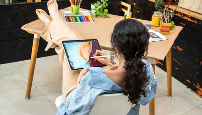 Utilizing blend modes Woman relaxing at a desk while painting on a tablet with a stylus, showcasing creative artwork made with digital watercolor brushes.
