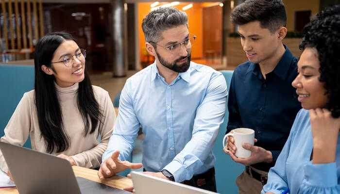 Employee development A diverse team of professionals collaborating around a laptop in a modern office, discussing business systems and workflow strategies.