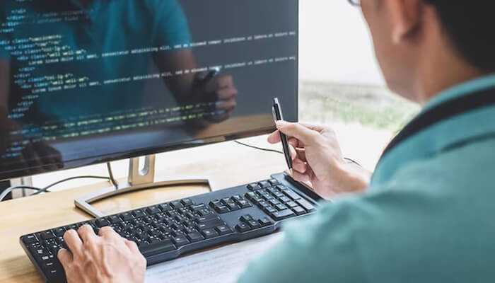 Coding test Image of a person participating in a coding test, reviewing code on a monitor while holding a pen, focused on programming tasks.