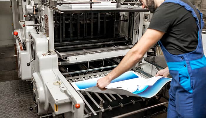 Misaligned prints - tycoonstory | tycoonstory media Uv printers showing misaligned prints as a technician adjusts printed sheets inside an industrial uv printing machine to correct alignment and print accuracy.