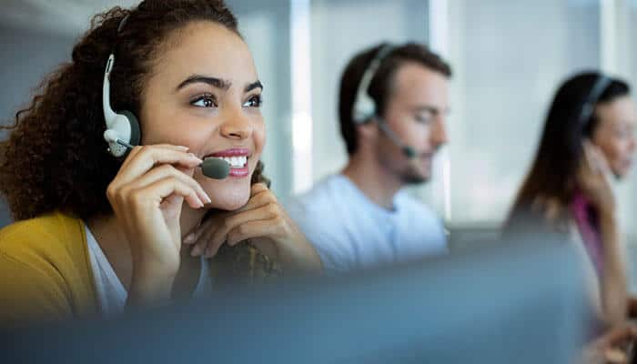 Customer-centric communication Support team member wearing a headset and smiling while assisting customers in a call center environment.