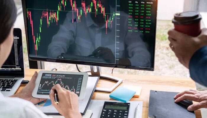 Uprofit reviews and ratings Two individuals reviewing stock market charts on multiple devices, with tablets and laptops showing uprofit review's trading analysis tools.