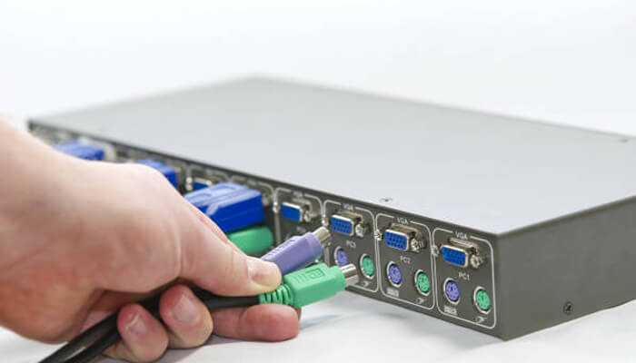 Using a kvm switch - tycoonstory | tycoonstory media Person connecting cables to a kvm switch to control two computers with a single set of peripherals.