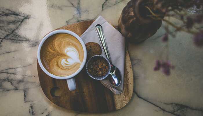Rustic Rustic coffee cup with latte art in the shape of a heart, accompanied by a spoon and a small serving of sugar on a wooden plate.
