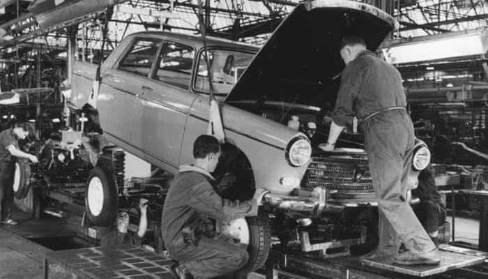 The car industrys future will significantly affect black america - tycoonstory | tycoonstory media Workers assembling a vintage car on a factory production line, showcasing early automotive manufacturing processes.