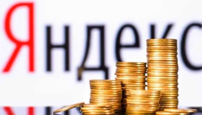 Yandex targets Stacks of gold coins in the foreground with the blurred russian name for yandex (Яндекс) in the background, symbolizing financial growth.