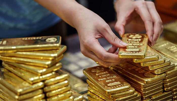 Gold in economic landscape Hands picking up a heavy gold bar from a large stack of ingots, illustrating the trade and value of gold in economic landscape.