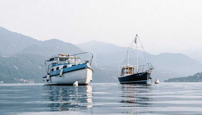 Ample design - tycoonstory | tycoonstory media Two boats anchored on calm water with mountains in the background resembling a duffy electric boat style.