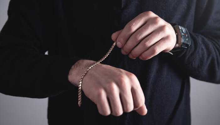 Man wearing a gold chain bracelet and a wristwatch on a black outfit, showcasing modern men's accessories Evolution of men's accessories