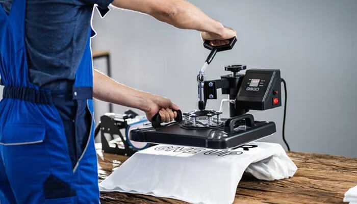 Print-on-demand A worker using a heat press machine to print on a white t-shirt displaying print-on-demand apparel production.