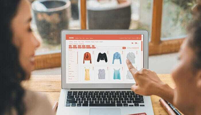 Adapt to trends in ecommerce - tycoonstory | tycoonstory media Two persons browsing an online apparel store on a laptop, discussing apparel, illustrating the aida model for ecommerce conversion.