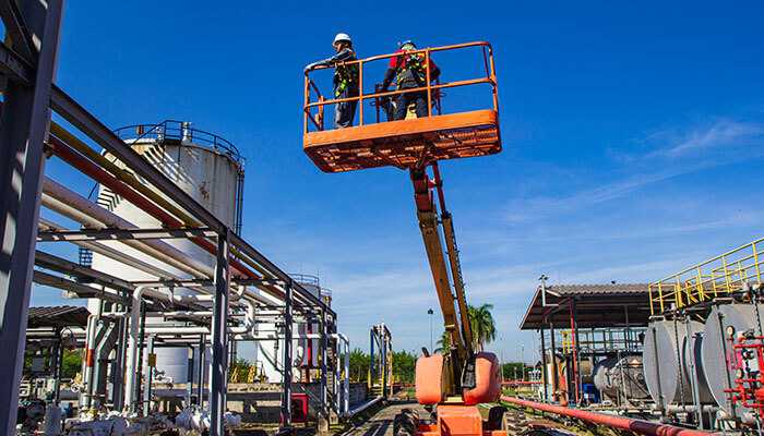 Aerial lift safety through training - tycoonstory | tycoonstory media Two workers wearing safety gear operating an aerial lift at a construction site, highlighting the importance of aerial lift safety in industrial settings.