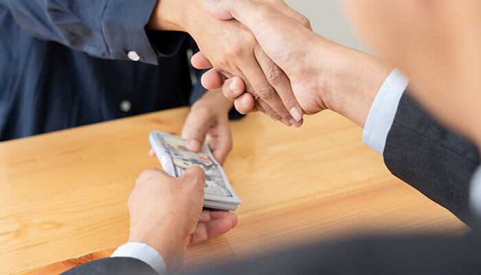 Best practices when borrowing from loved ones - tycoonstory | tycoonstory media Handshake with cash exchange, representing the pros and cons of borrowing from loved ones and friends in a personal loan or financial agreement.