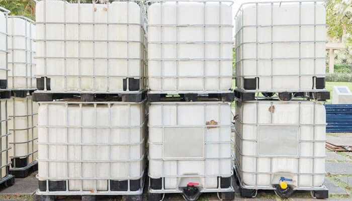 Clean and maintain totes for safe reuse - tycoonstory | tycoonstory media Large industrial used ibc totes containers stacked vertically with a metal cage for transporting or storing bulk liquids.