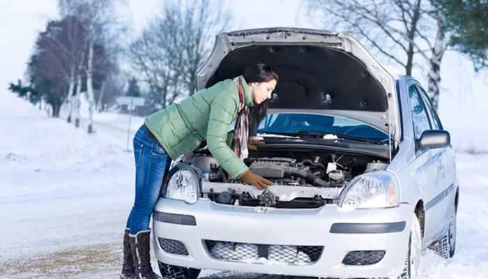 Person inspecting a car engine in a snowy environment, illustrating how cold climates impact vehicle performance and how location affects car value. Location affects car value
