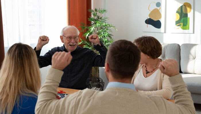 Creating a safe and comfortable environment for seniors - tycoonstory | tycoonstory media An old man joyfully celebrates with family members around the table, showing joyful moments in elder support and family caregiving